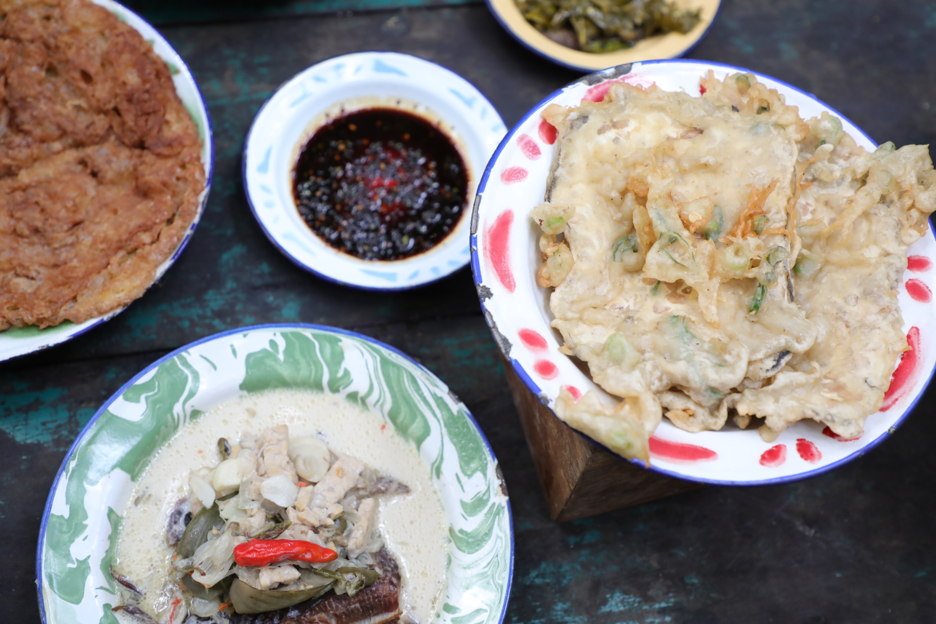 Overhead photo of Folony food dishes and spice accompaniments on a textured table.